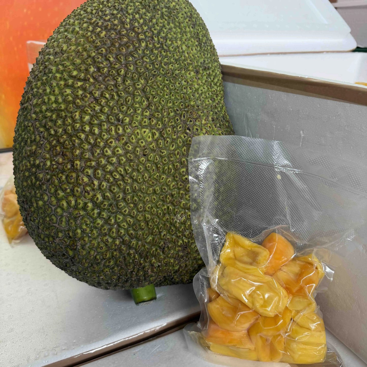 A whole green jackfruit next to a vacuum-sealed bag of fresh, bright yellow jackfruit pods.