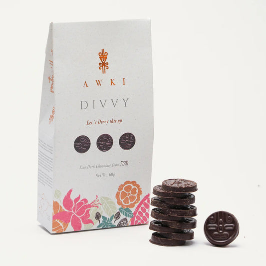 A stack of AWKI Divvy 75% dark chocolate coins next to eco-friendly white packaging with ancestral floral designs.
