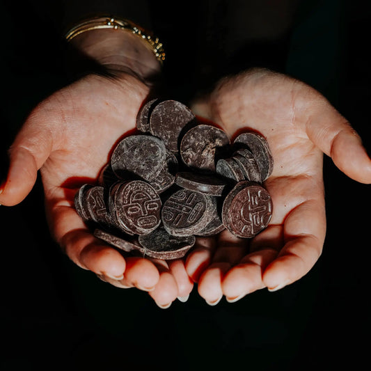 A person holding a handful of dark, ceremonial-grade cacao chunks embossed with ancient Ecuadorian patterns against a dark background.