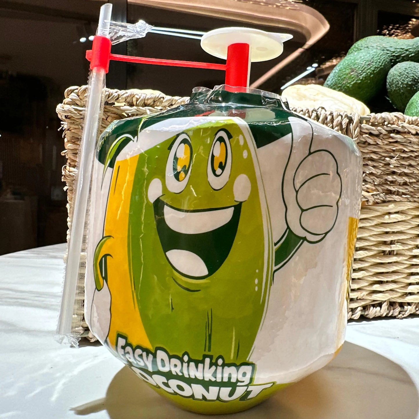 A fresh young drinking coconut in white protective packaging with a built-in opening tool and straw, ready to drink.