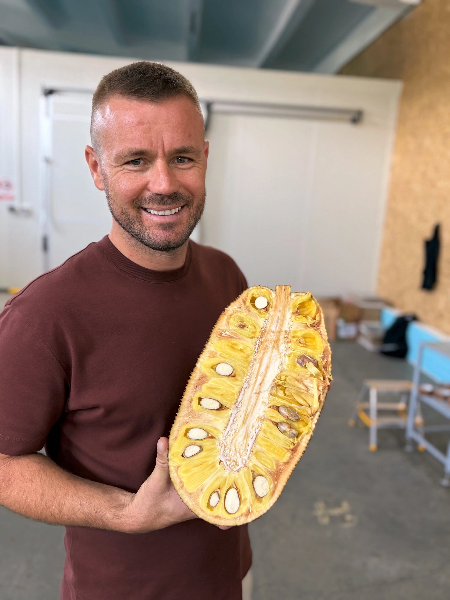 A Iulian Perseca holding a halved fresh jackfruit showing large yellow edible pods and white seeds.