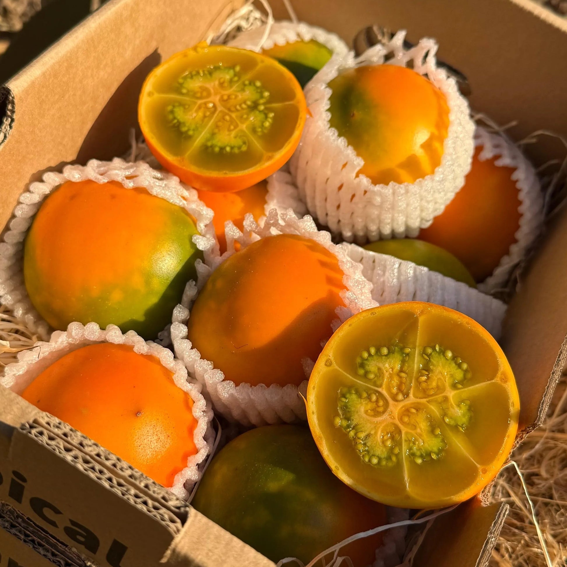 A box of fresh orange lulo fruits (naranjilla), with two halves sliced open to reveal the characteristic juicy green citrus-like pulp and seeds.