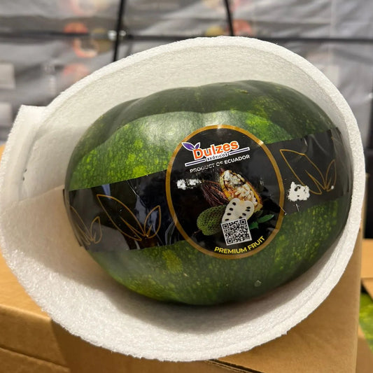 A top-down view of large, grey-green Zapallo Macre squash in a box on hay, with one sliced open to reveal thick, bright orange flesh.