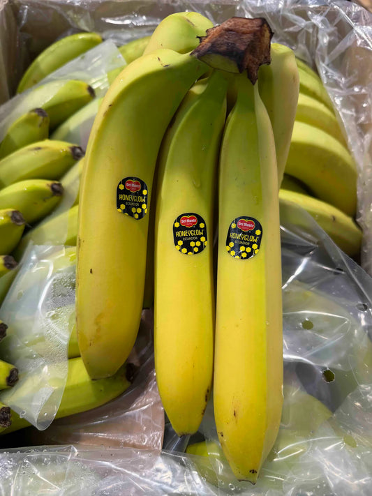 A bunch of bright yellow Honeyglow bananas from Ecuador with black and gold Del Monte premium labels