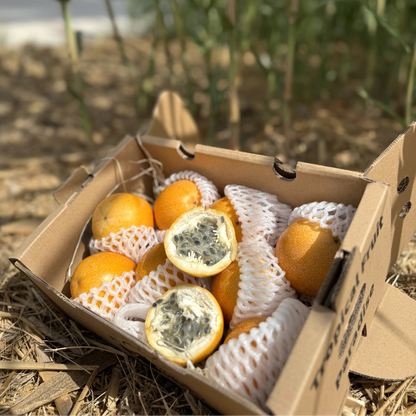 A box of ripe orange sweet granadillas on hay, with one fruit sliced open to reveal the translucent, jelly-like sweet pulp and edible grey seeds.