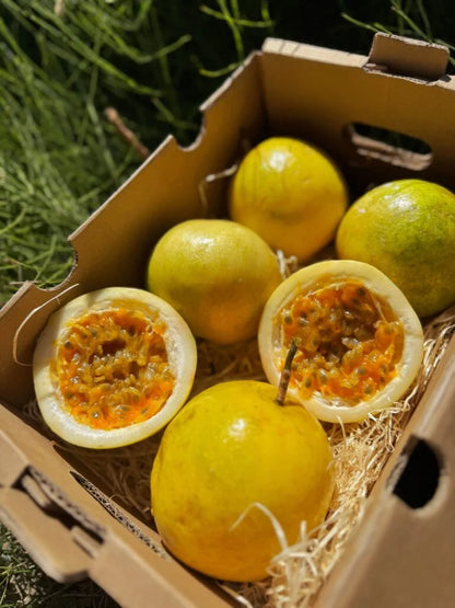 Fresh yellow passion fruits (maracuya) from Vietnam in a box, with one sliced open to show the juicy golden pulp and edible black seeds.